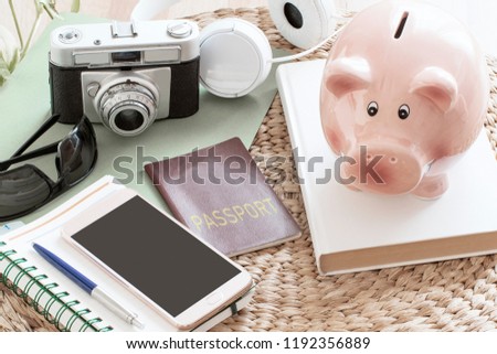 Piggy bank next to a passport, a smartphone, a camera and some stuff ready for a touristic travel. Empty copy space for Editor's text.