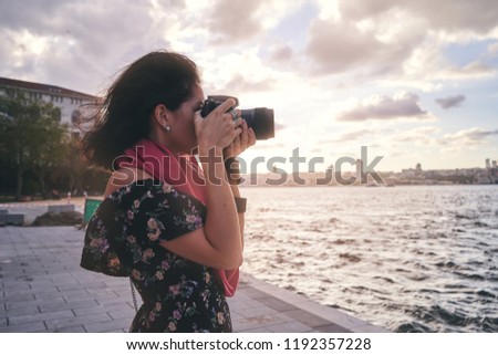 Woman photographer with red scarf, taking pictures of landscape near sea at sunset
