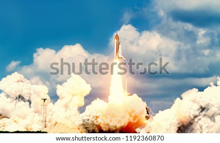 Launch of the spaceship from the spaceport by day. Space shuttle in clouds of smoke on the background of dramatic sky. Some elements of this image are furnished by NASA Royalty-Free Stock Photo #1192360870