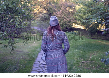 Woman in gray cap and coat standing in autumn nature.