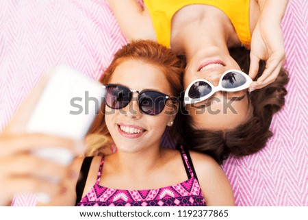 summer fashion, eyewear and leisure concept - smiling teenage girls in sunglasses lying on picnic blanket taking selfie