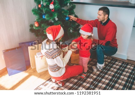 Merry Christmas and Happy New Year. Attractive picture of cute and nice family. They decorating Christmas tree. Young woman holds toy with small girl. Man puts blue toy on tree.