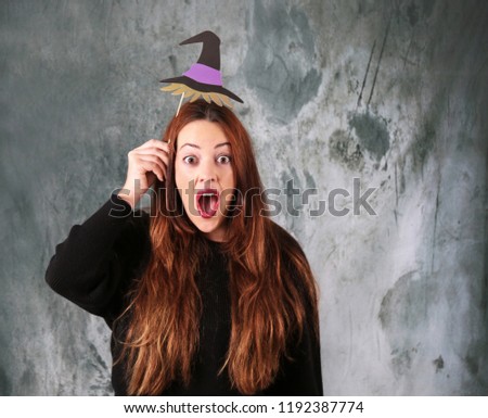 Surprised young woman wearing a halloween purple witch hat against a grunge background
