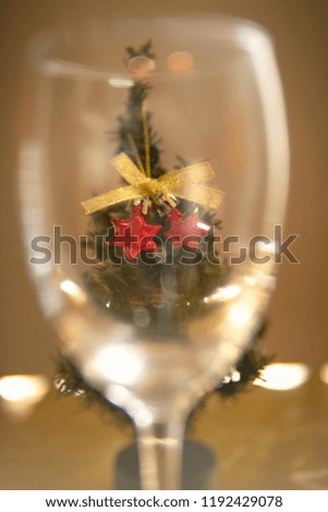 Peering through an empty wine glass at a small Christmas tree at Christmas time with gold background. Vertical picture