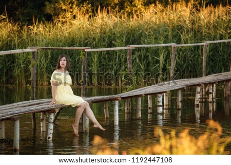 Young girl sitting on the wooden bridge, splashing with legs