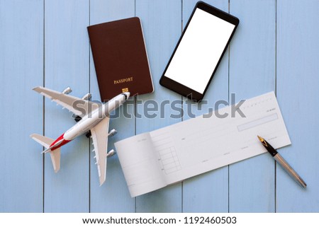 Mockup image of checkbook, pen, mobile smartphone with empty screen, passport and airplane model on blue wooden background.Trip and travel, business technology concept.Payment by cheque. clipping path