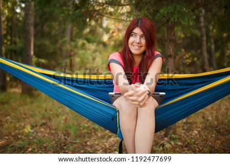 Photo of woman looking in camera with laptop sitting in hammock
