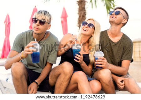 three friends on the beach spend fun while drinking cocktails at sun