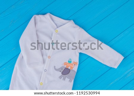 White soft wool baby pajama with print. Blue wood background.