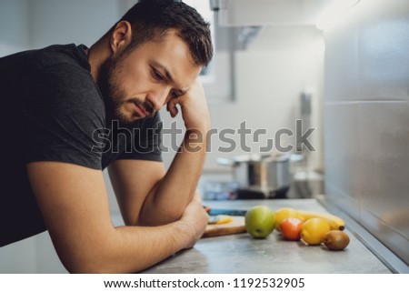 Sad man leaning on the kitchen countertop and looking down