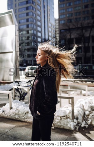 Young girls develop hair in the wind. Girl in a black fur coat. Autumn, cold, street, fashion
