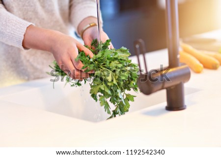 Picture of adult woman washing parsley in the kitchen
