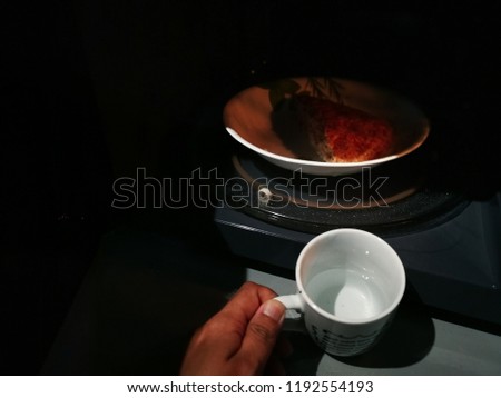 Water in cup is placed in the microwave together with the bread to make it moist and fluffy while reheating it.