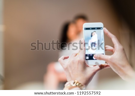 a woman holding smartphone in hand, taking photography romantic scene pre-wedding of couple in studio. Happy Anniversary, Wedding, Love celebrate and phone concept with copy space.