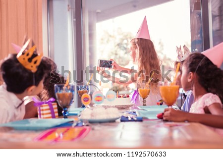 Taking photos. Long haired careful girl standing with modern smartphone and taking selfies with her friends at the party
