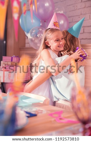 Sweet hug. Cheerful birthday girl smiling happily and feeling thankful while holding lovely present and hugging her mother