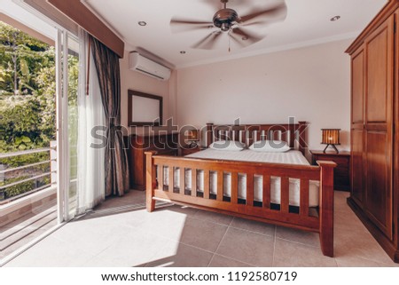 Luxury house or penthouse bedroom room interior with a wooden bed and huge view windows with a patio overlooking the jungle
