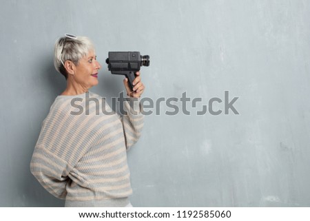 senior cool woman with a vinatge video camera against grunge cement wall.