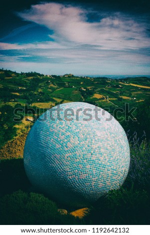 Giant blue and white tiles ball surrounded by nature on top of a hill with landscape view on the background. No people.