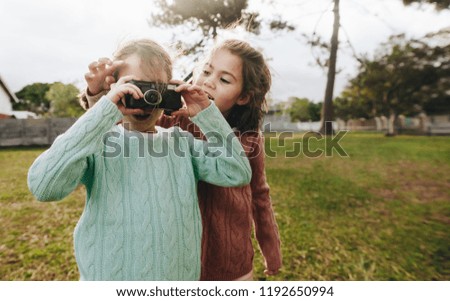 Little girl taking pictures using camera at the park with her sister. Two little girls taking photographs using camera at the playground.