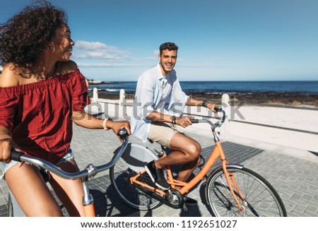 Happy man and woman moving around the city on bicycles. Young couple having fun riding bicycles in street with sea in the background.