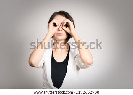 beautiful girl makes binoculars with her hands, plans, short haircut, isolated over the background