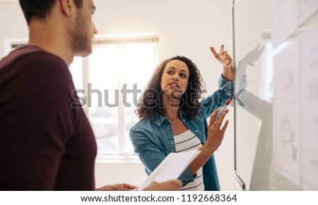 Woman entrepreneur discussing business ideas and plans on a board in office. Businesswoman writing on a whiteboard and explaining while her colleague is listening.