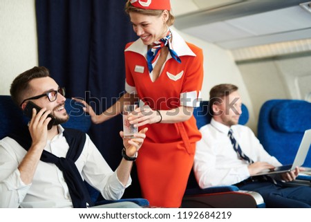 Portrait of smiling flight attendant serving glass sparkling water to handsome businessman enjoying first class trip, copy space Royalty-Free Stock Photo #1192684219