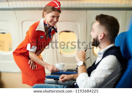 Portrait of smiling flight attendant serving coffee to young businessman in first class, copy space Royalty-Free Stock Photo #1192684225