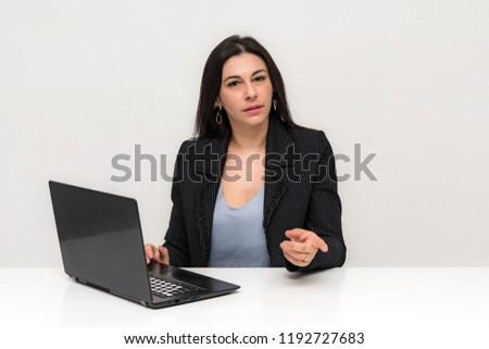 Portrait of a beautiful brunette woman on a white background with different emotions sitting at a table with a laptop. She is right in front of the camera in various poses.