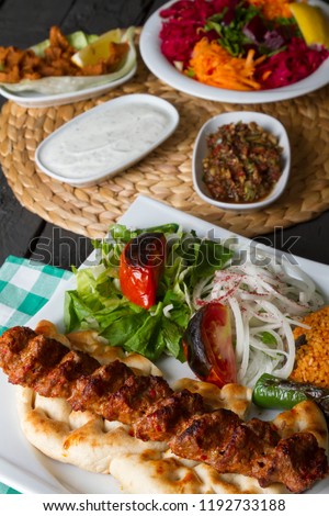 Turkish and Traditional Adana Kebab serving with salad, onion, pepper and bulgur on rustic black wood table. Dark photography concept with copy space.