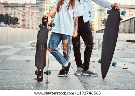 Cropped photo of a trendy dressed young couple posing with skateboards near a skyscraper.
