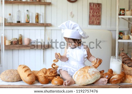  child in the form of a cook in the kitchen is mowing bread, bread, bagels, next to flour and various bread bakeries