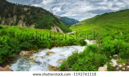 Georgian nature landscape in Svaneti region with mountain river in highlands. Green hills and mountains covered by grass. Cloudy sky over village Adishi on horizon, Georgia