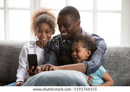 Happy African family spending time have a fun together using mobile phone at home. Black father with little daughter and son make selfie photo picture watching video sitting on couch at sitting room