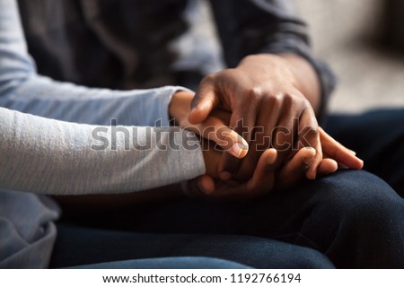 Close up black woman and man in love sitting on couch two people holding hands. Symbol sign sincere feelings, compassion, loved one, say sorry. Reliable person, trusted friend, true friendship concept