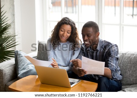 African black positive married couple sitting on sofa at home read documents paper checking bills, bank account balance feeling satisfied and happy. Refund income last loan payment good news concept Royalty-Free Stock Photo #1192766221