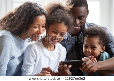 Close up black family with small children have a fun sitting on couch together at home. Happy american married couple little preschool adorable daughter and son watching funny video using smartphone