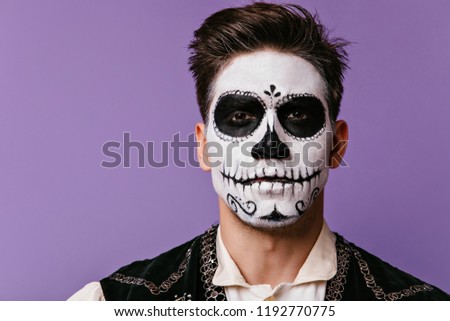 Close-up portrait of brunette man with traditional mexican halloween makeup. Studio photo of scary caballero celebrating day of the dead.