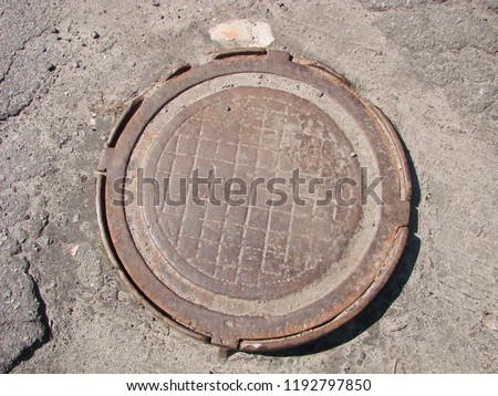 An old sewer manhole cover surrounded by an asphalt street