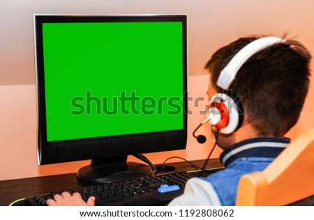 A young gamer boy playing video games on computer wearing headphones and colorful keyboard