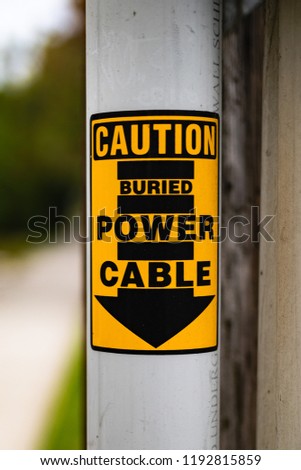 A black and yellow caution sign warns of a buried power cable. 