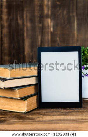 Ebook, digital tablet device, with old real books nearby on the rustic background