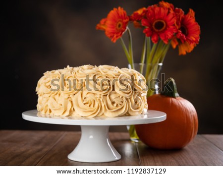Horizontal image of a Pumpkin Spice Cake with red-orange flowers and a small pumpkins.