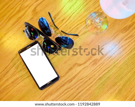 Phone and a couple glasses. Modern black smart phone with white isolated display for mockup in wooden table. Cocktail, glasses.