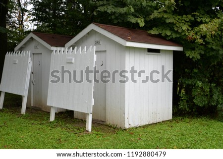 Girls and boys outhouse bathrooms in bright white with brownish red roofs out in the back of the lot. 