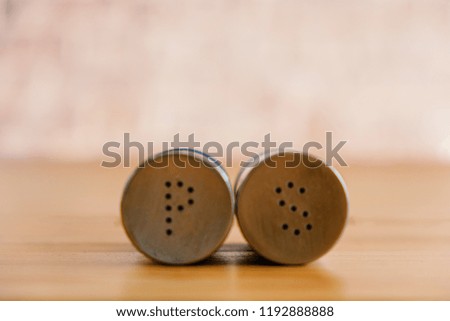 Metal pepper shaker and salt shaker lying near each other on wooden table