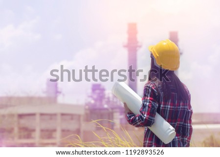 Read view of Engineering asian woman standing with yellow safety helmet and blue print in hand against oil refinery in petrochemical Aerial view oil. Industrial zone,Energy power station Background.