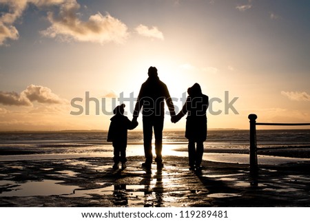 Silhouette of two adults and a child at the coast