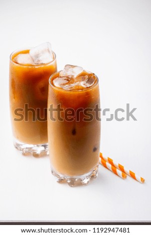 Ice coffee in a tall glass with cream poured over and coffee beans. Cold summer drink on white background with copy space